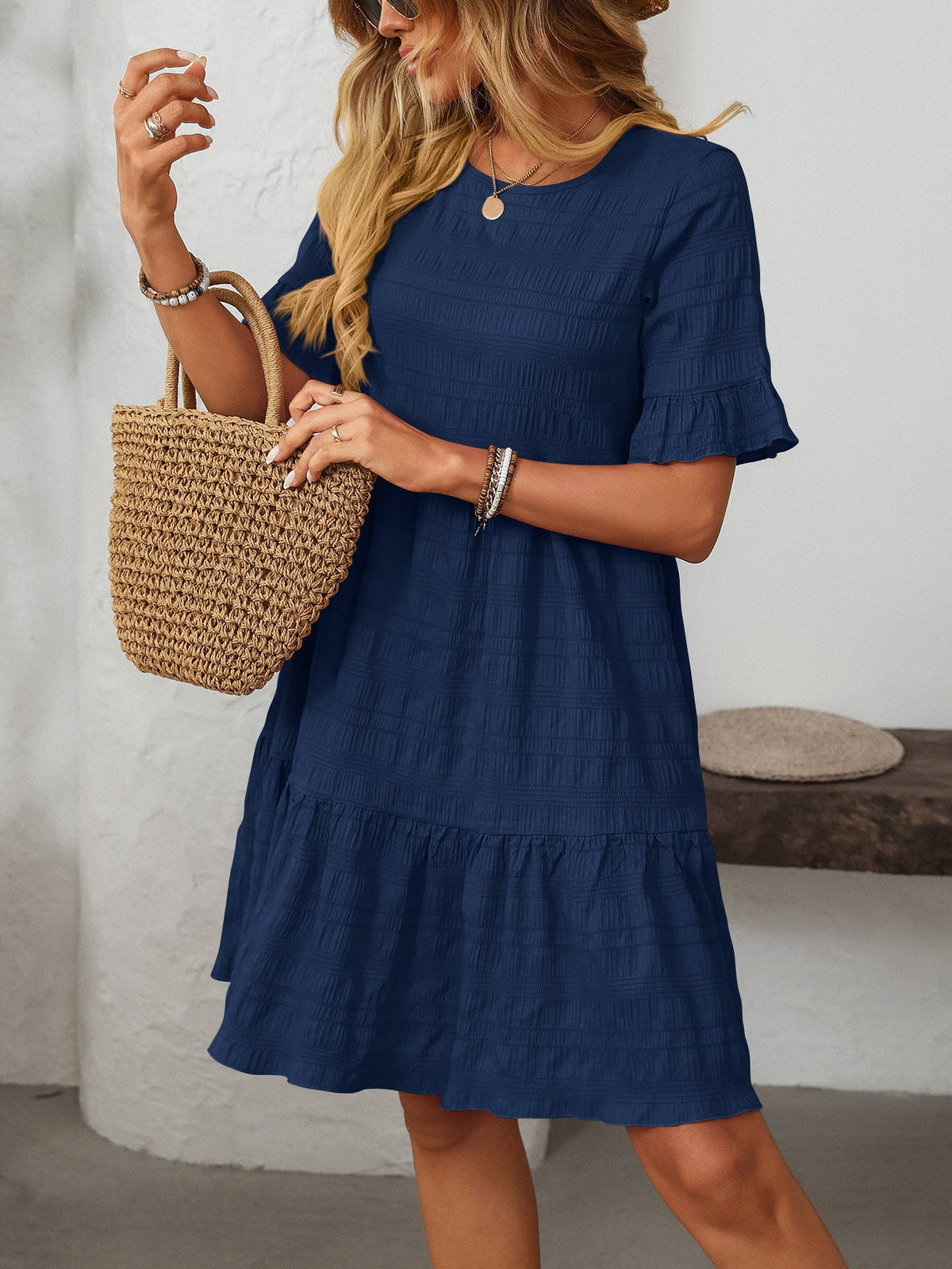 Margo & Main – Vianne navy blue textured tiered short-sleeve dress, three-quarter front view with a straw tote and arm raised, US women's sizes