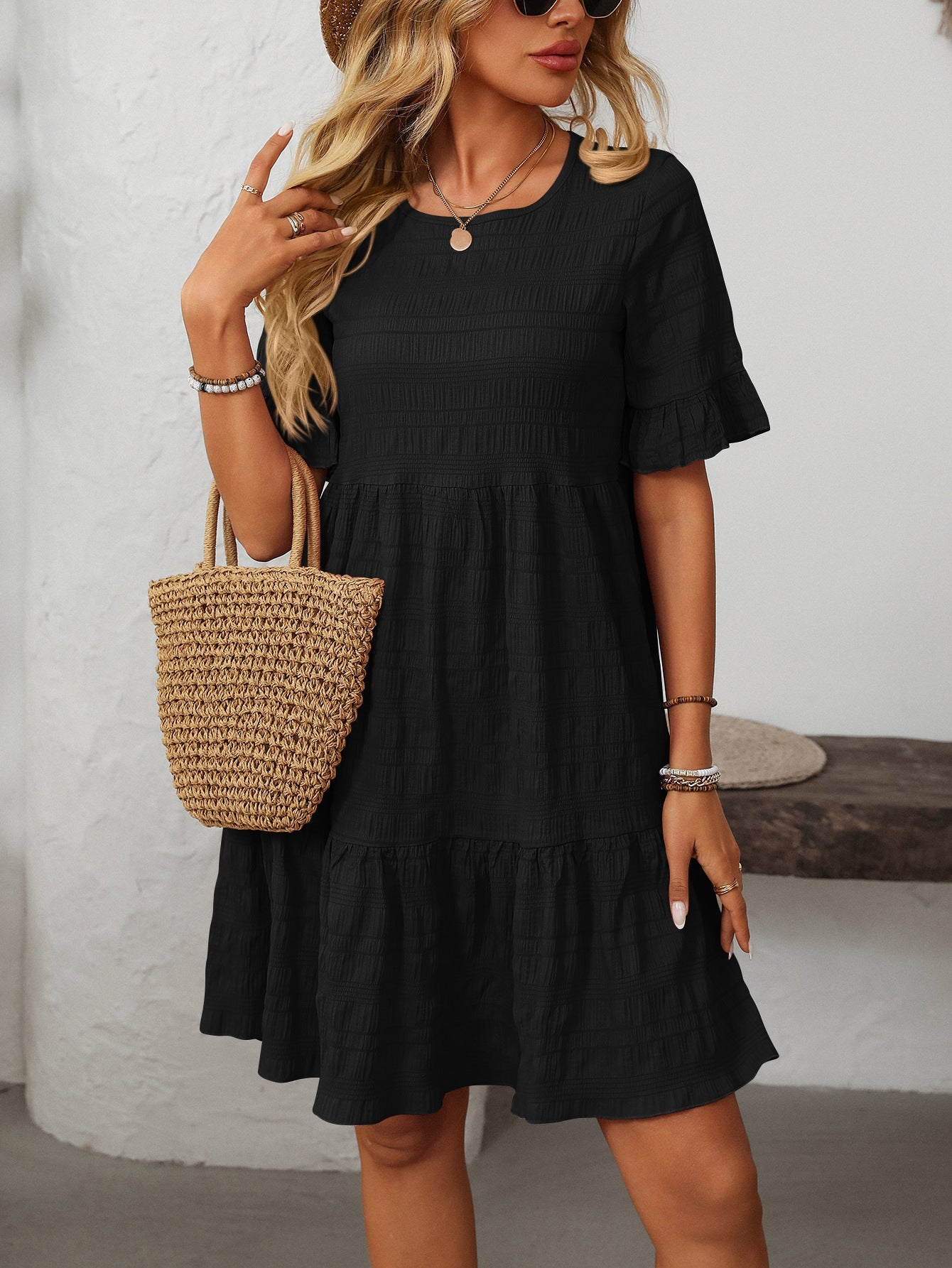 Margo & Main – Vianne black textured tiered short-sleeve dress, front view with a straw tote at the hip, US women's sizes