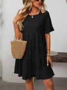 Margo & Main – Vianne black textured tiered short-sleeve dress, front view with a straw tote at the hip, US women's sizes