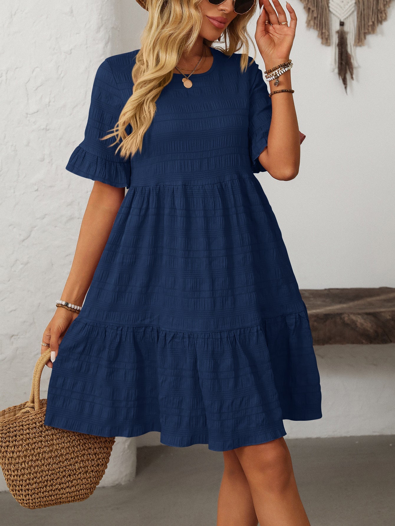 Margo & Main – Vianne navy blue textured tiered short-sleeve dress, front view with a straw tote and hand raised to hair, US women's sizes