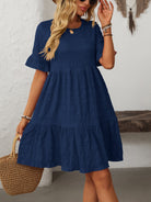 Margo & Main – Vianne navy blue textured tiered short-sleeve dress, front view with a straw tote and hand raised to hair, US women's sizes