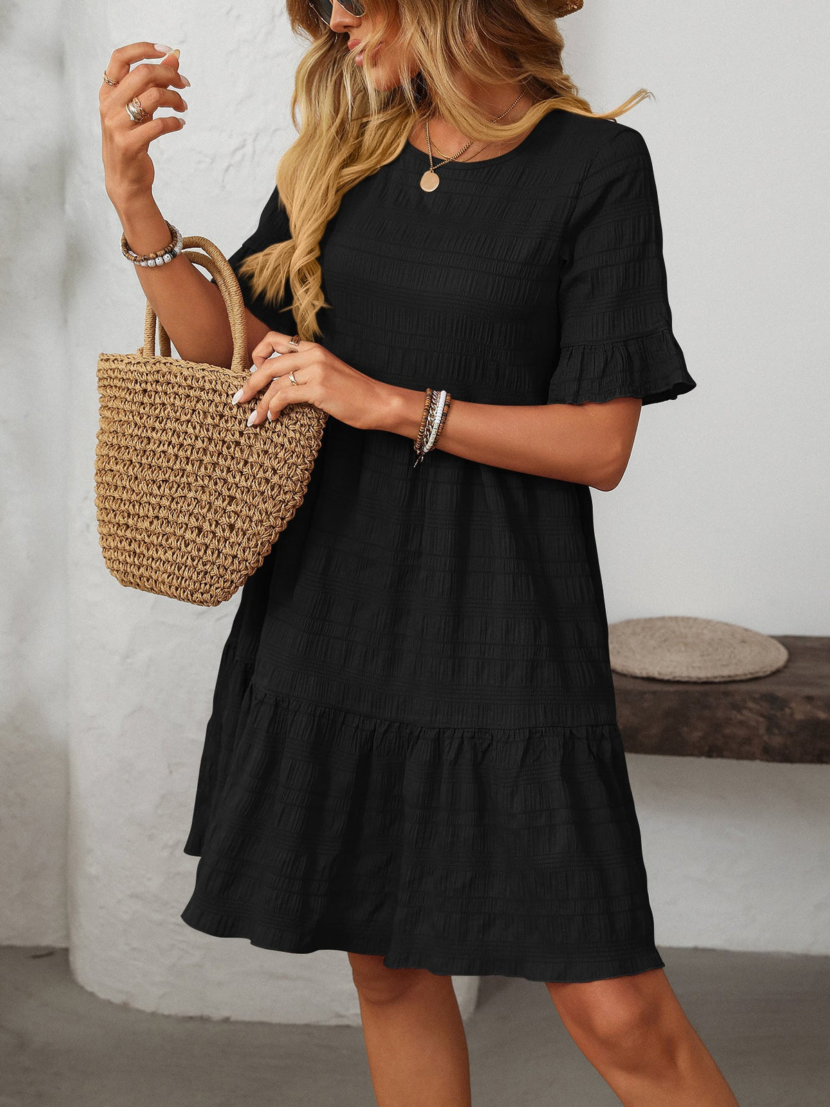 Margo & Main – Vianne black textured tiered short-sleeve dress, front view with a straw tote on the forearm, US women's sizes