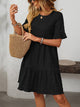 Margo & Main – Vianne black textured tiered short-sleeve dress, front view with a straw tote on the forearm, US women's sizes